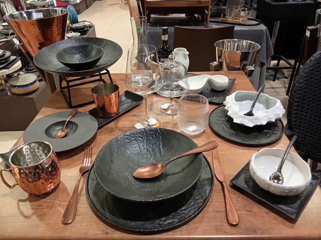Mesa con vajilla negra, cuencos y piezas de cobre